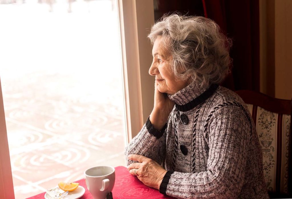 old woman looking out window thinking about the benefits of independent senior living