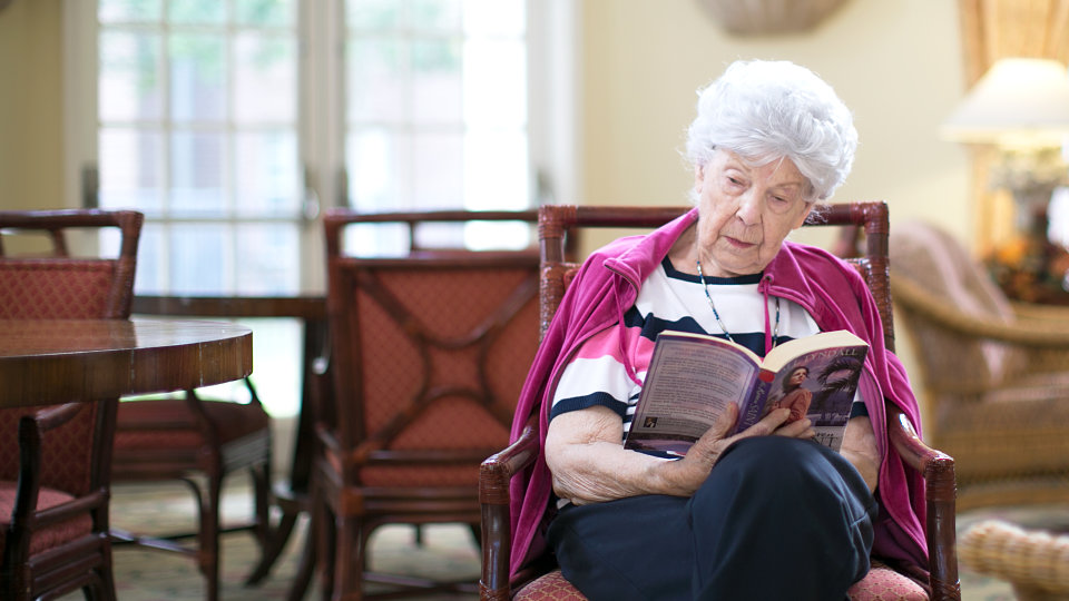 older woman in chair reading a book