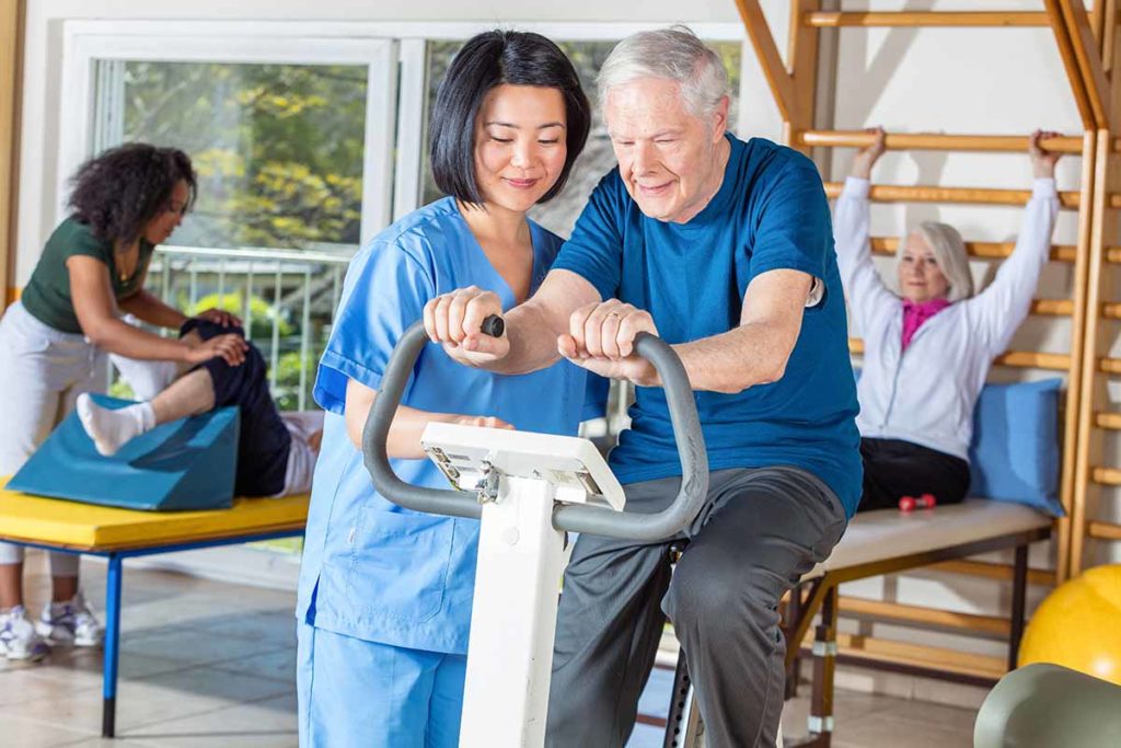 a woman helping a man on an elliptical as one of the types of rehab therapy for seniors