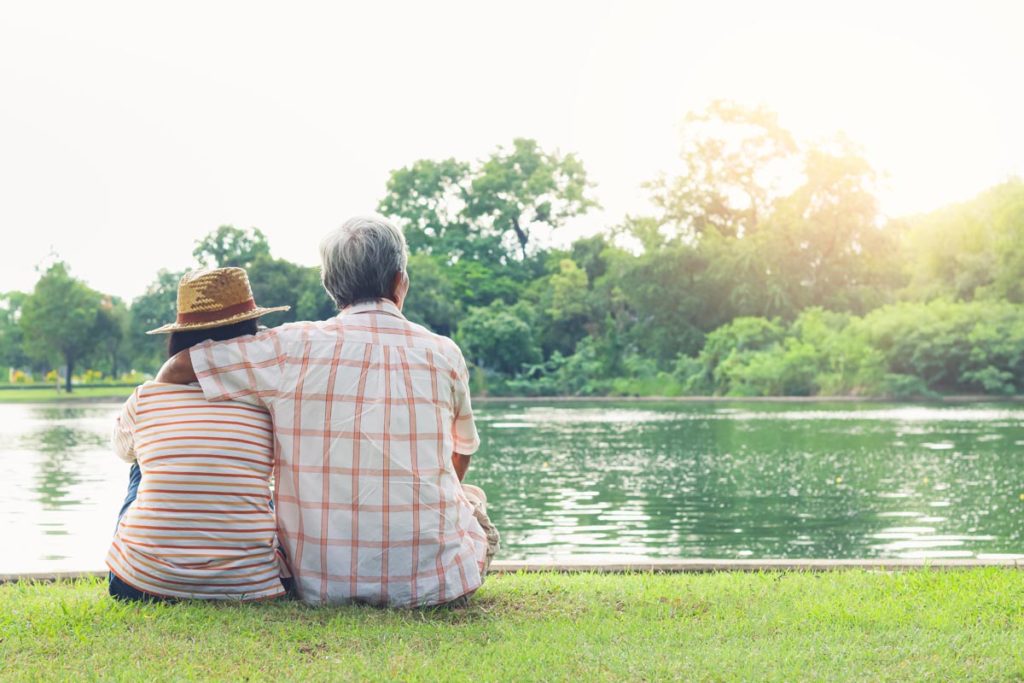 Senior adults sitting on grass by pond, pondering retirement community living
