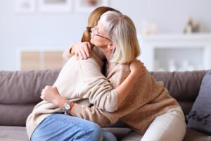 Woman hugs mother on couch as she talks about seeking alzheimer's care