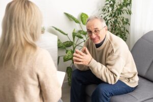 A man seeking mental health resources for seniors sits on a couch, speaking to a therapist.